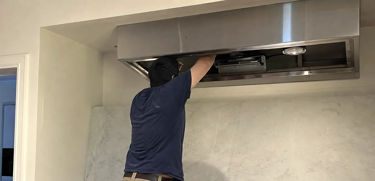 Close view of an open hood canopy with an arm reaching inside it, the marble splashback behind