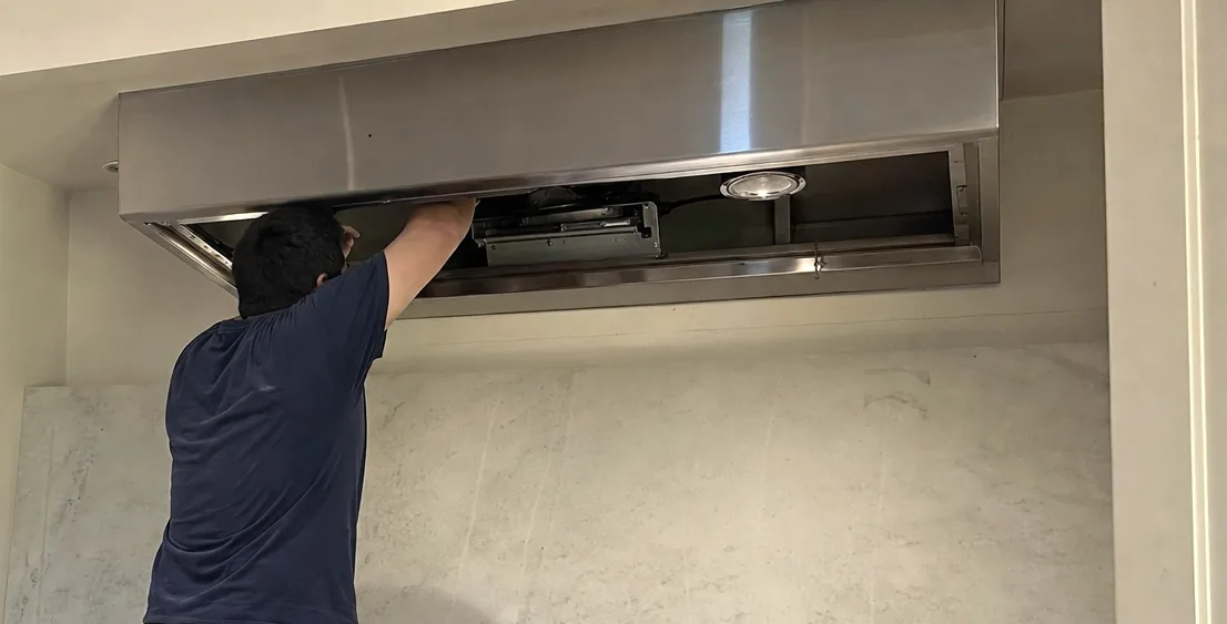 A hood canopy opened for service, the blower housing and wiring visible above the range below