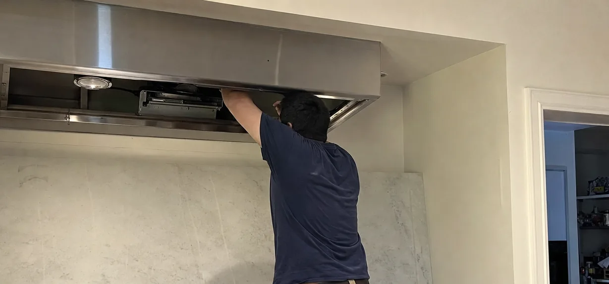 A technician working inside an open hood canopy, filters removed and stacked on the counter beside him