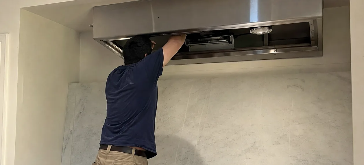 The open underside of a stainless ventilation hood mid-service, its baffle filters lifted out